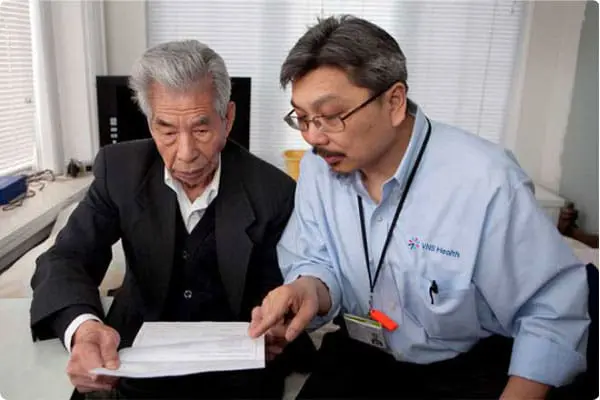 A VNS Health team member helping an elderly patient with paperwork.