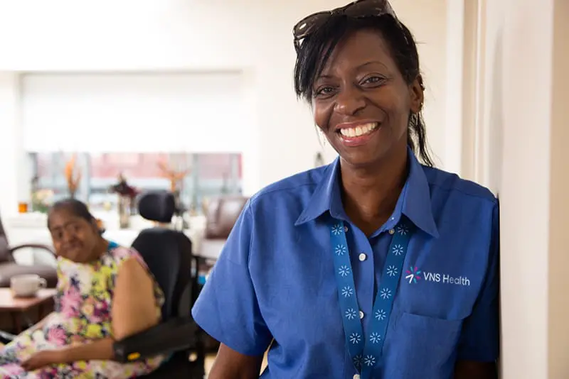 VNS Health Team Member Giselle Harris smiles in front of her patient.