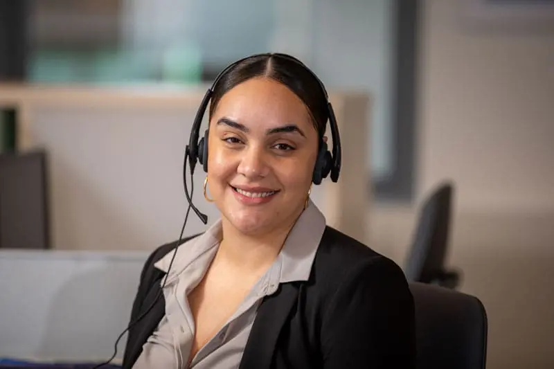 Smiling VNS Health call center team member wearing a headset, seated at a desk in an office environment.