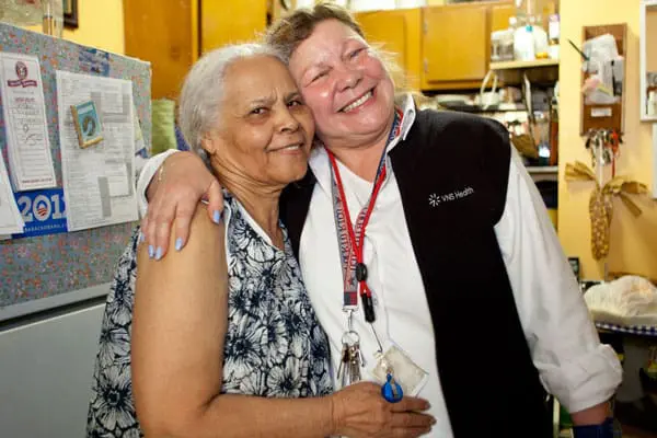 A VNS Health home health aide hugging her patient and smiling.