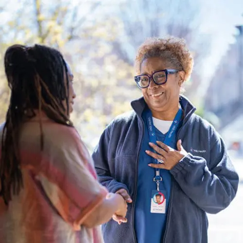 A VNS Health home health aide greeting a patient's family member at the door.