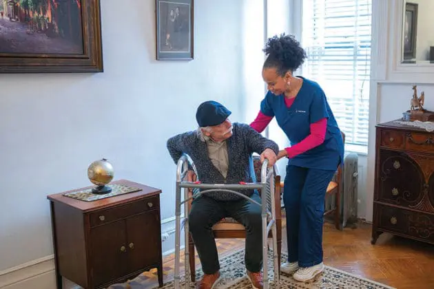 A VNS Health home health aide helping a patient with a walker.