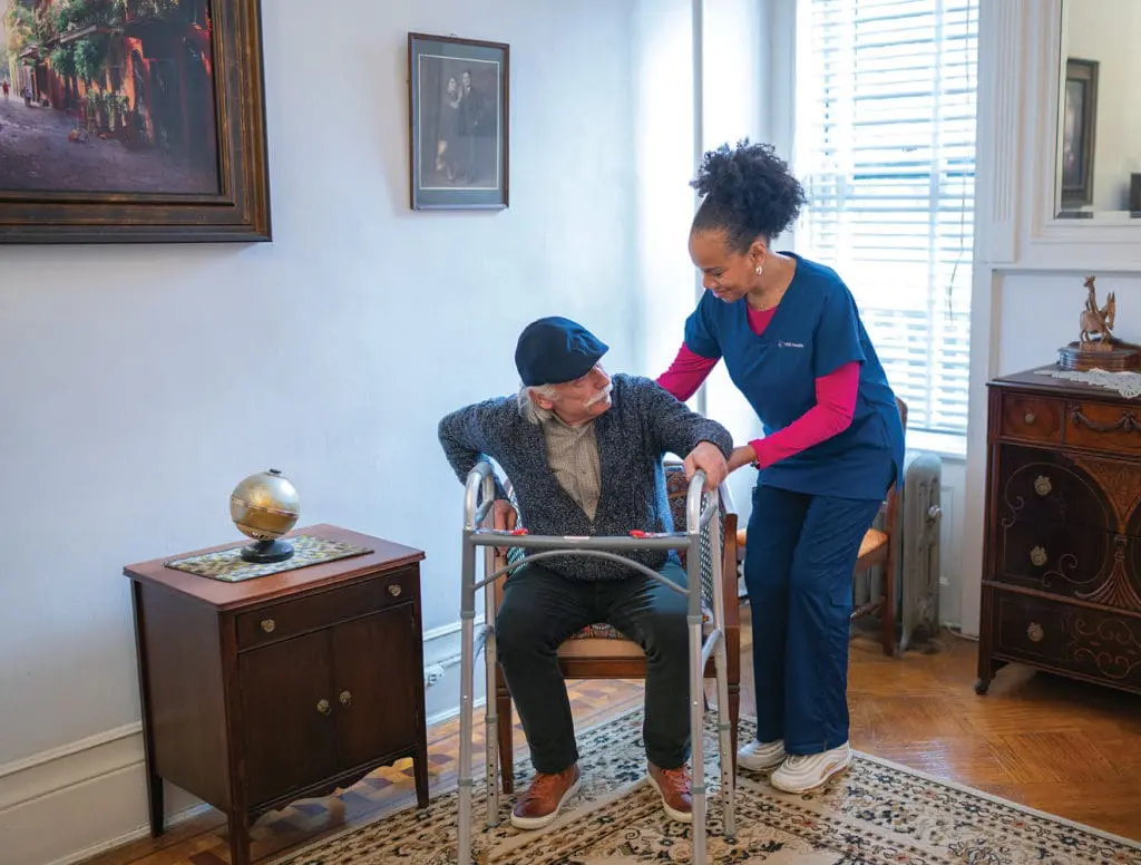 A VNS Health home health aide helping a patient with a walker.