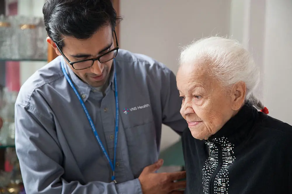 A VNS Health home health aide helps his elderly patient stand up.