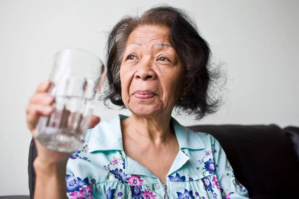An elderly woman drinking a large glass of water.