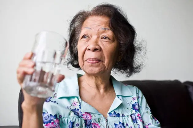 An elderly woman drinking a large glass of water.
