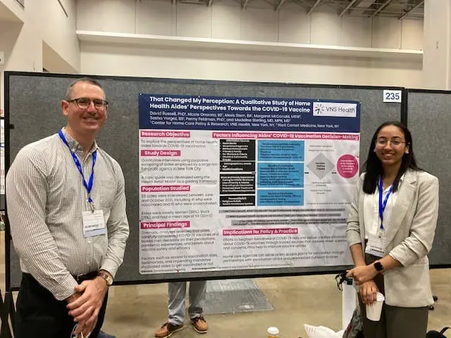 Two VNS Health Research Center team members standing in front of a research infographic.