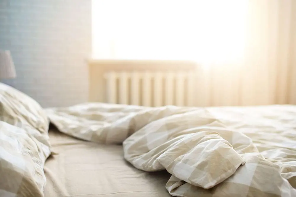 A beige unmade bed in the morning.