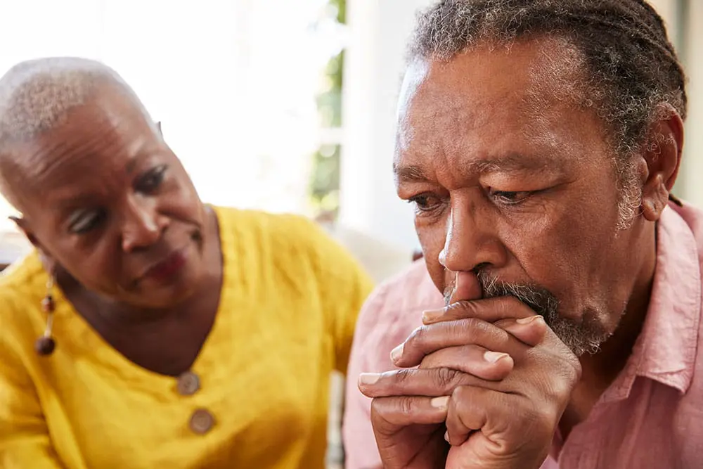 A caregiver looking at frowning man.