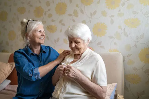A caregiver holding the shoulders of an elderly woman.