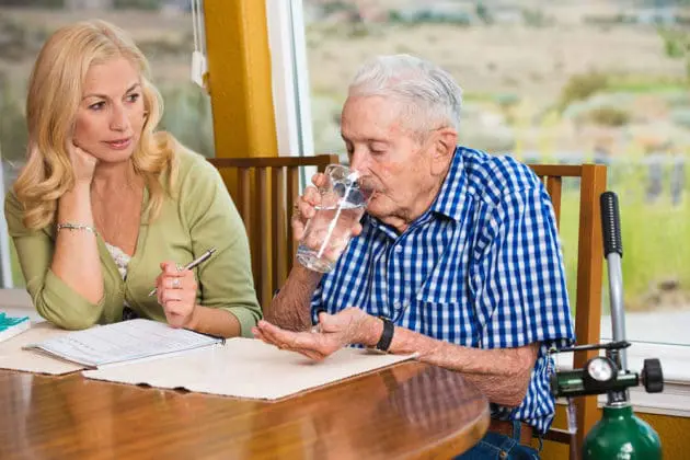 An adult daughter watching her elderly father take medicine.