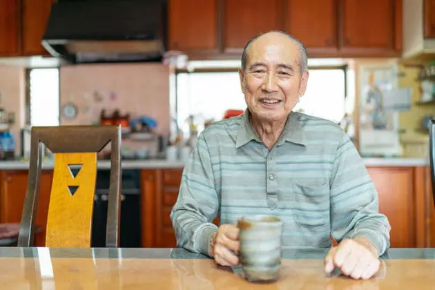 An elderly man sitting at a table holding a mug.