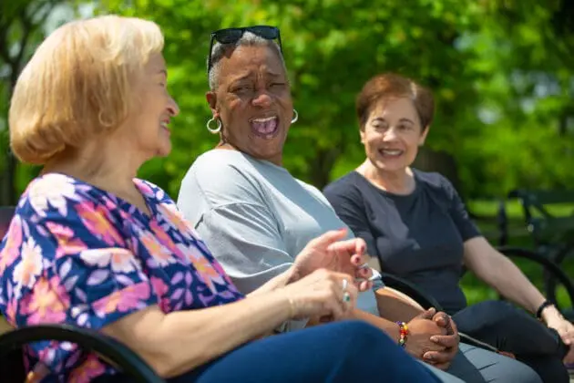 three women sitting on a bench talking and laughing