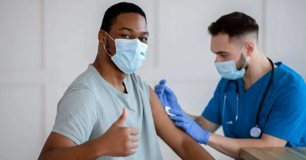 A patient giving a thumbs up while receiving a flu shot from a nurse.