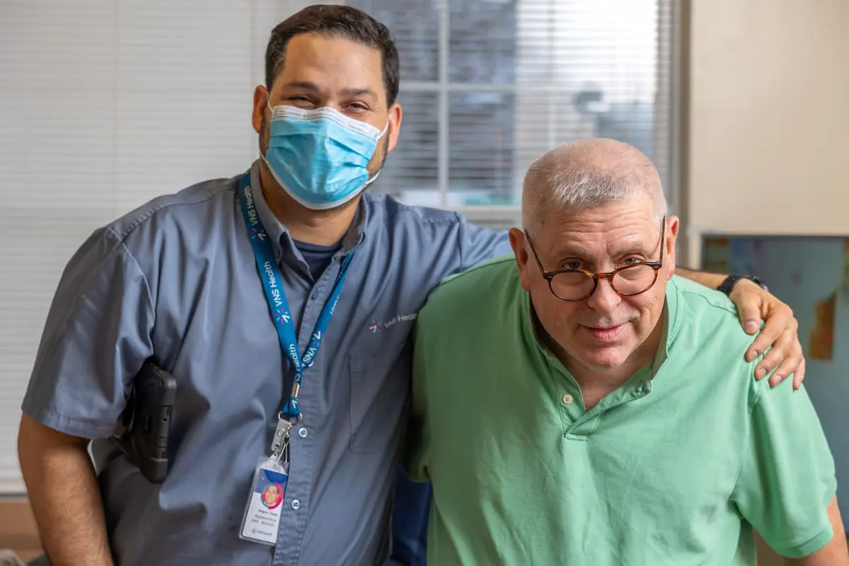 A VNS Health home health aide standing next to his patient.