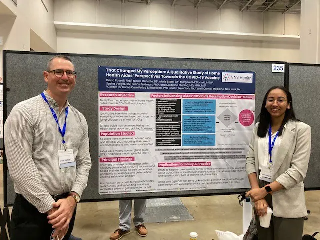 Two VNS Health Research Center team members standing in front of a research infographic.