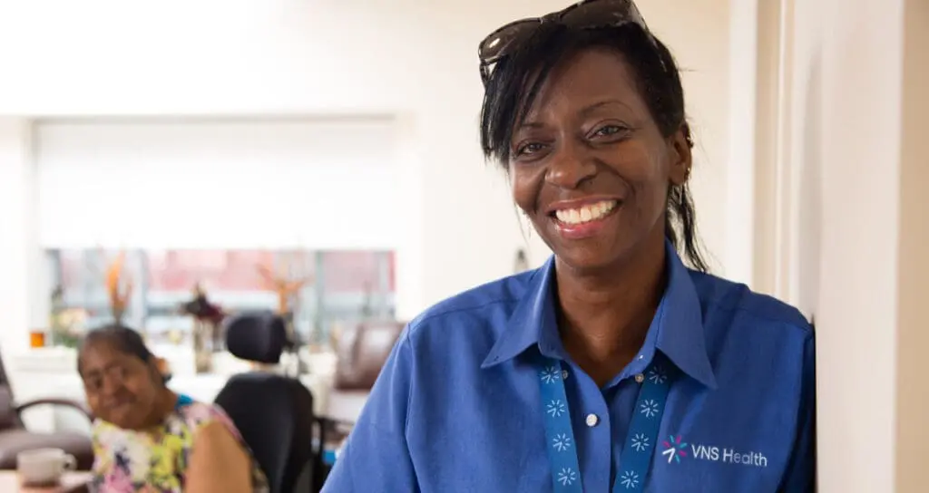 VNS Health Team Member Giselle Harris smiles in front of her patient.
