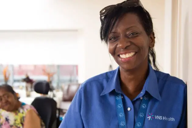 VNS Health Team Member Giselle Harris smiles in front of her patient.