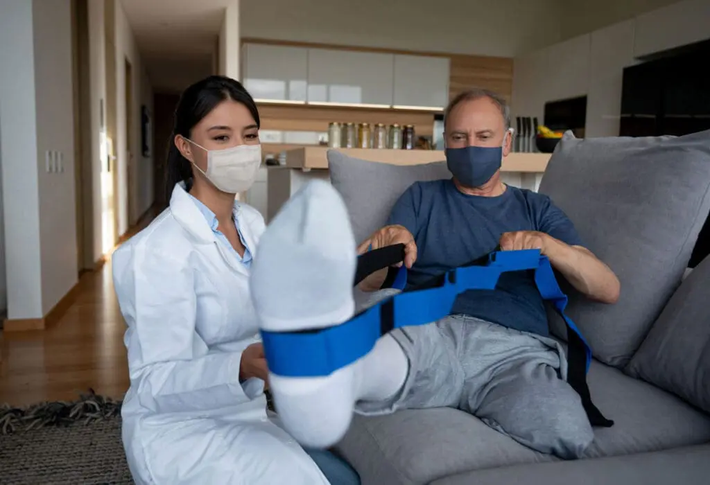A VNS Health Physical Therapist assists her patient with leg exercises using a resistance band.