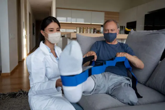 A VNS Health Physical Therapist assists her patient with leg exercises using a resistance band.