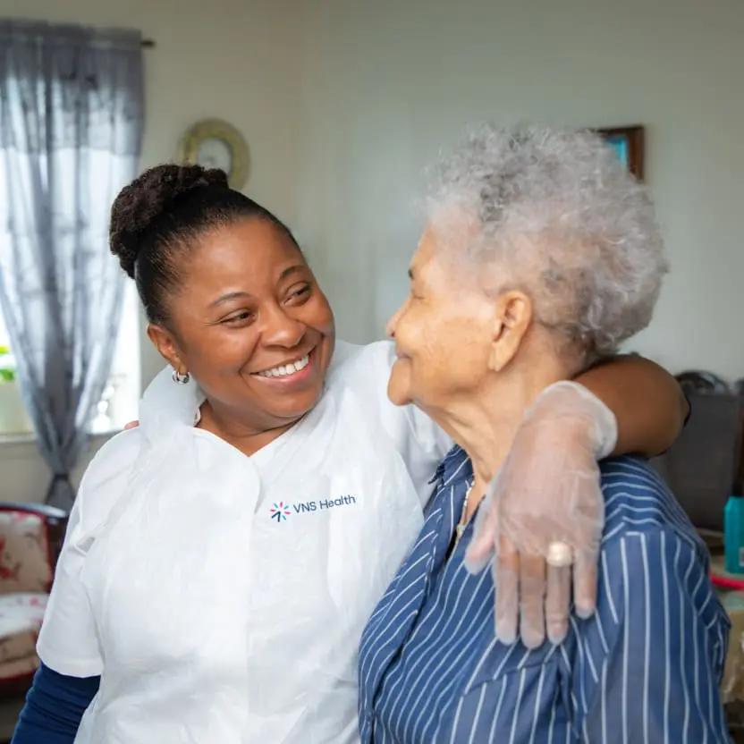 A VNS Health home health aide stands with her arm around her patient.