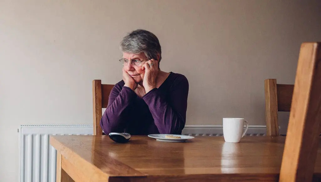 An elderly woman sitting alone at a kitchen table.