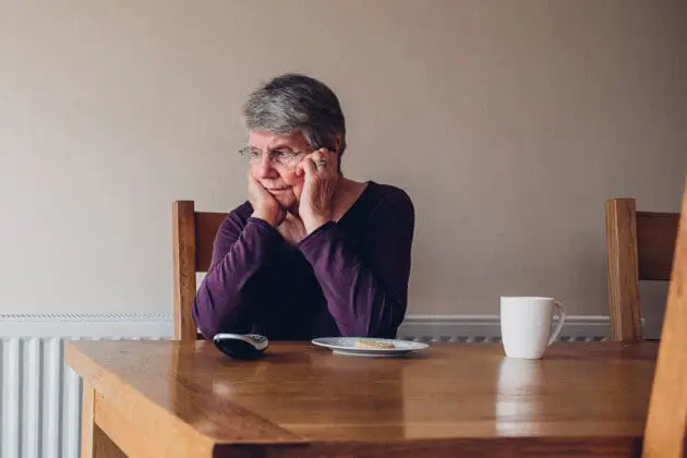 An elderly woman sitting alone at a kitchen table.