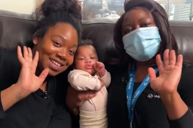 VNS Health Nurse-Family Partnership patient Rachel holds up her baby with help from nurse Jasmine.