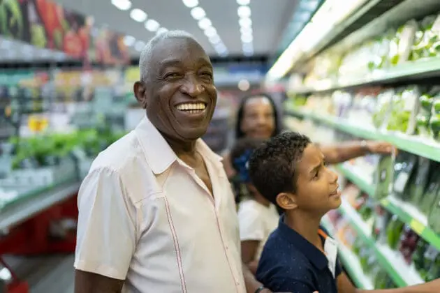 An elderly man smiling in the grocery store with his son.