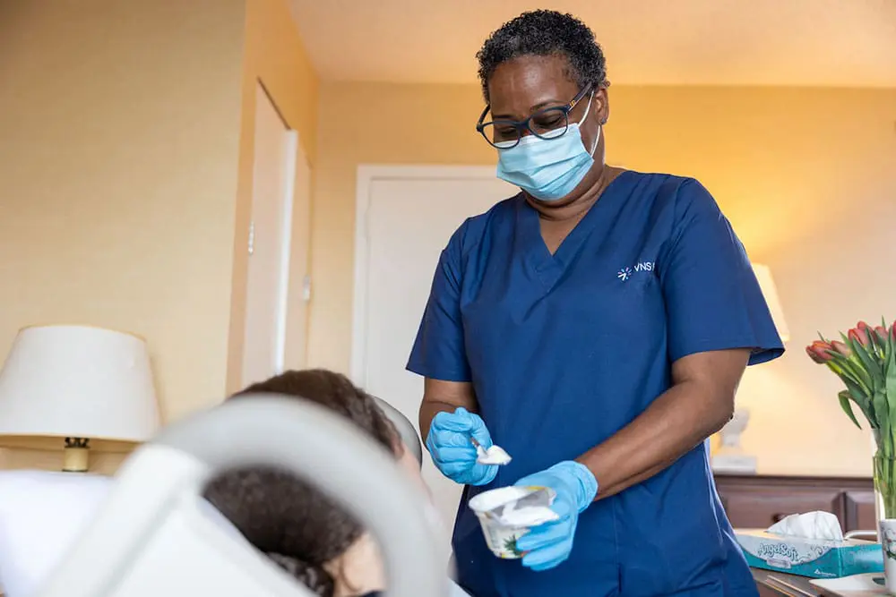 A VNS Health hospice home health aide standing at her patient's bedside.