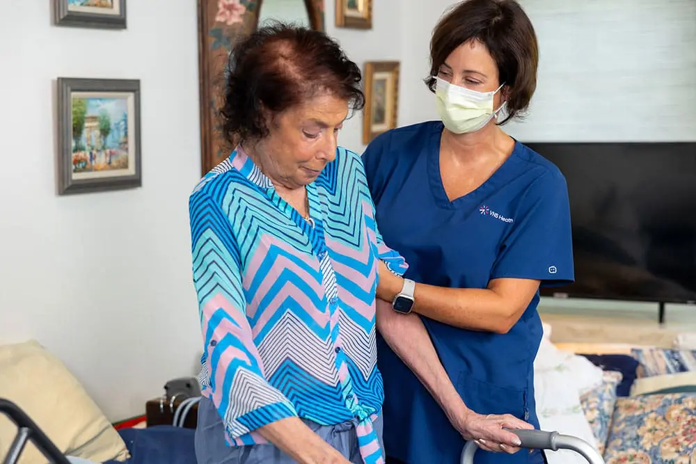 A VNS Health home health aide helping her patient walk.