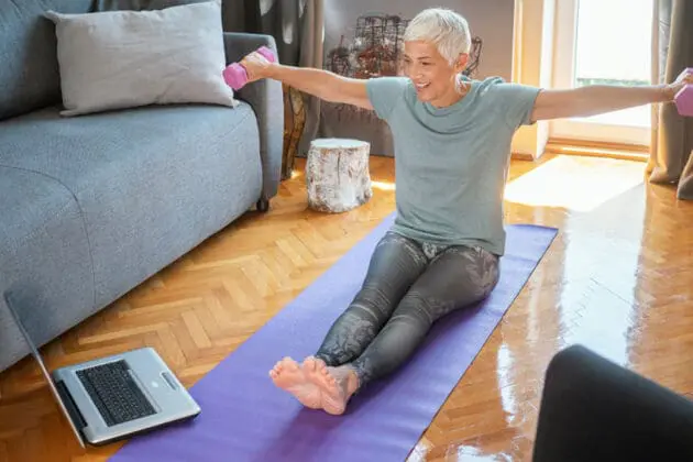 An elderly woman lifting weights in her home.