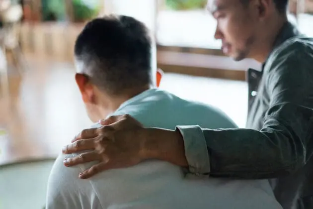 An adult son placing his arm around his elderly father's back.