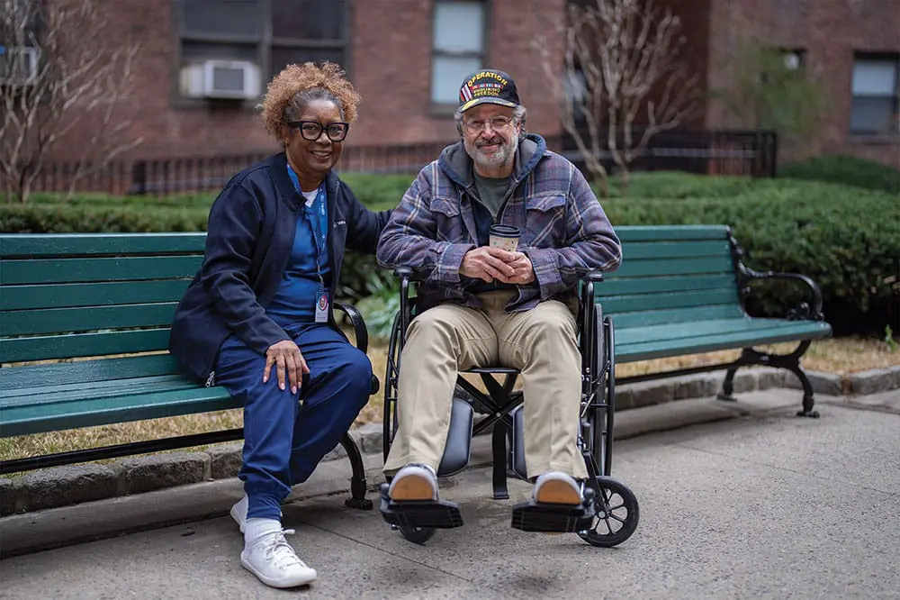 A VNS Health home health aide sitting outside with a Veteran patient.