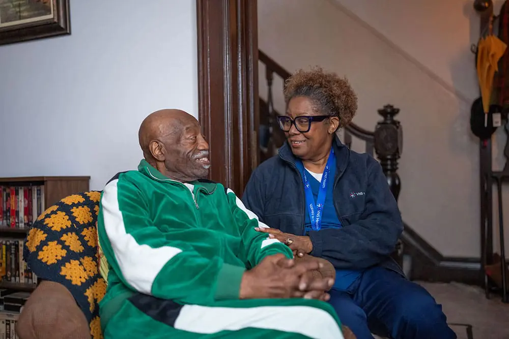 A VNS Health home health aide sitting next to her patient.