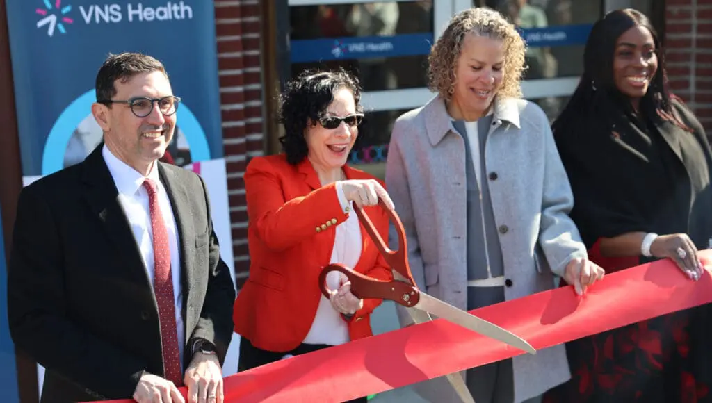 VNS Health team members and elected officials smiling before cutting red ribbon.