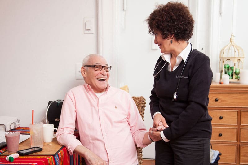 vns health team member standing and holding hand of sitting senior man
