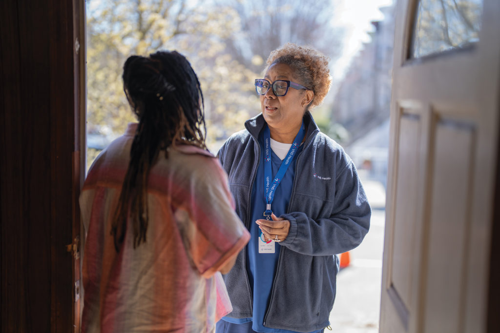 An adult woman greets the VNS Health team member at the door as she arrives for a first home care visit.
