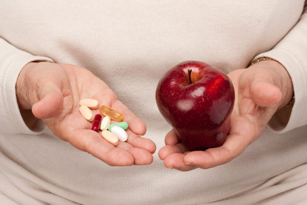 A senior holds pills in one hand and an apple in the other.