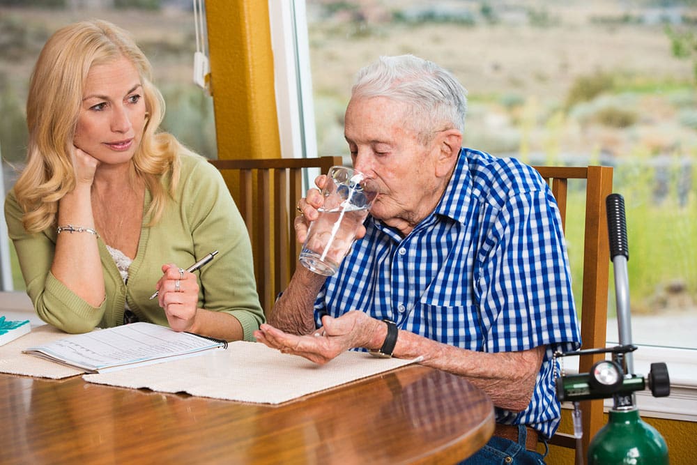 adult daughter watching elderly father take medicine