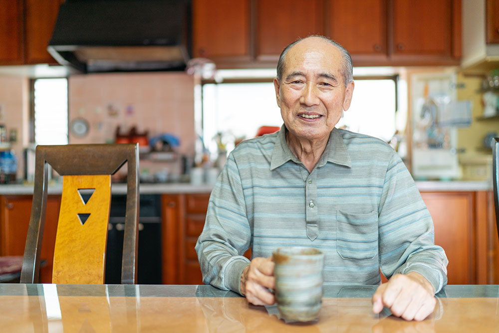elderly man sitting at table holding cup