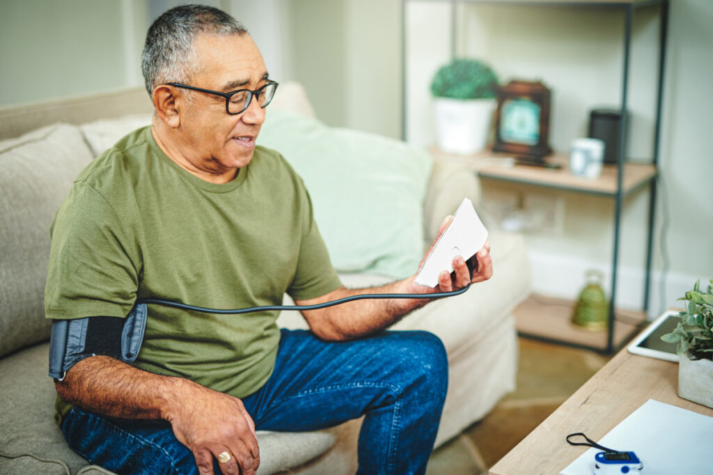 older adult sitting on a couch and checking blood pressure