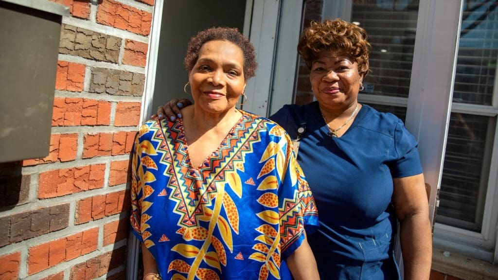 Picture of home health aide Marie Dorviline with her client, Yanick standing outside of Yanick's front door.