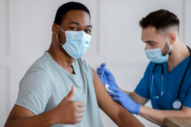 man giving a thumbs up while getting vaccine from a nurse
