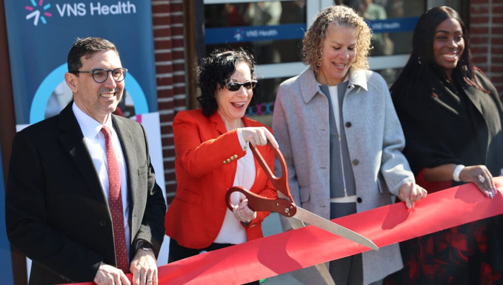 VNS Health team members and elected officials smiling before cutting red ribbon.