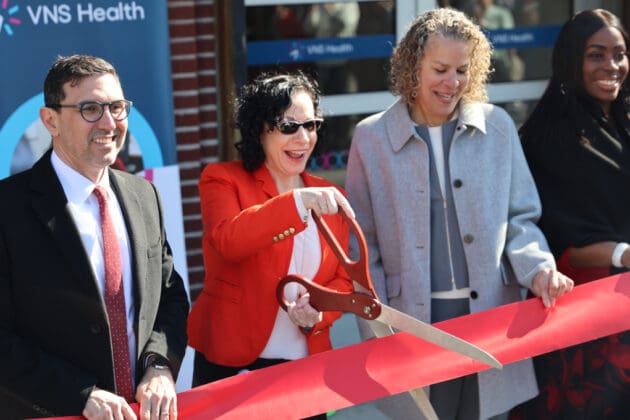 VNS Health team members and elected officials smiling before cutting red ribbon.