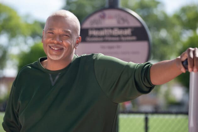 Older male adult leaning on a railing and smiling.